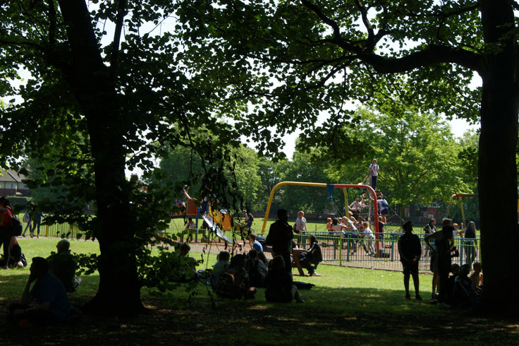 A play area, with some people sat in front of it and others playing in it. 